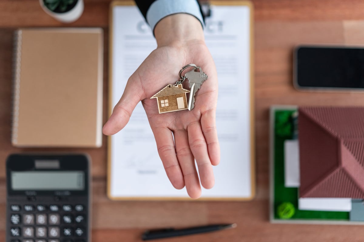 Top view key on real estate agent hand over wooden table surrounded by calculator and legal document as symbolic for house loan or mortgage