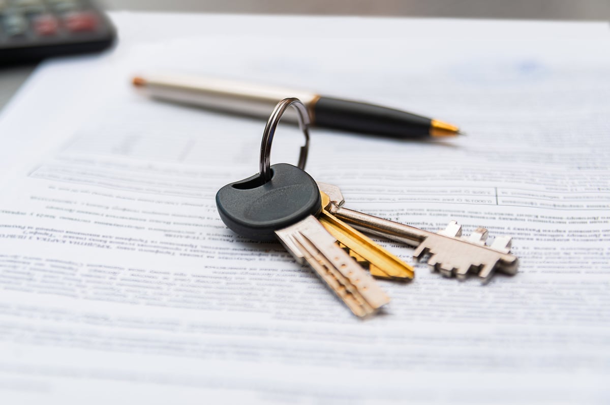 A set of keys on a ring rests on printed documents with a pen nearby, suggesting signing, contracts, or real estate paperwork in a professional office setting.