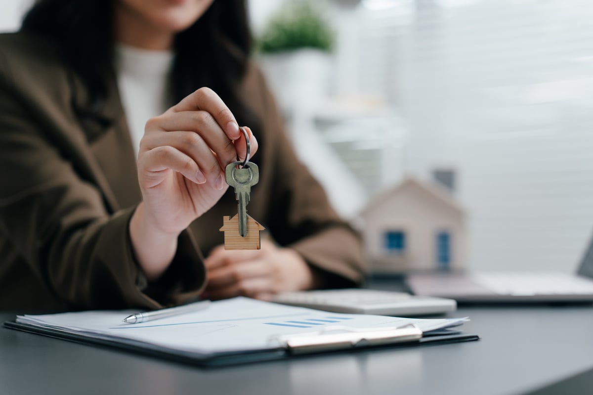 Woman holding a house key at office desk with documents, real estate agent handing over key to new home buyer or owner